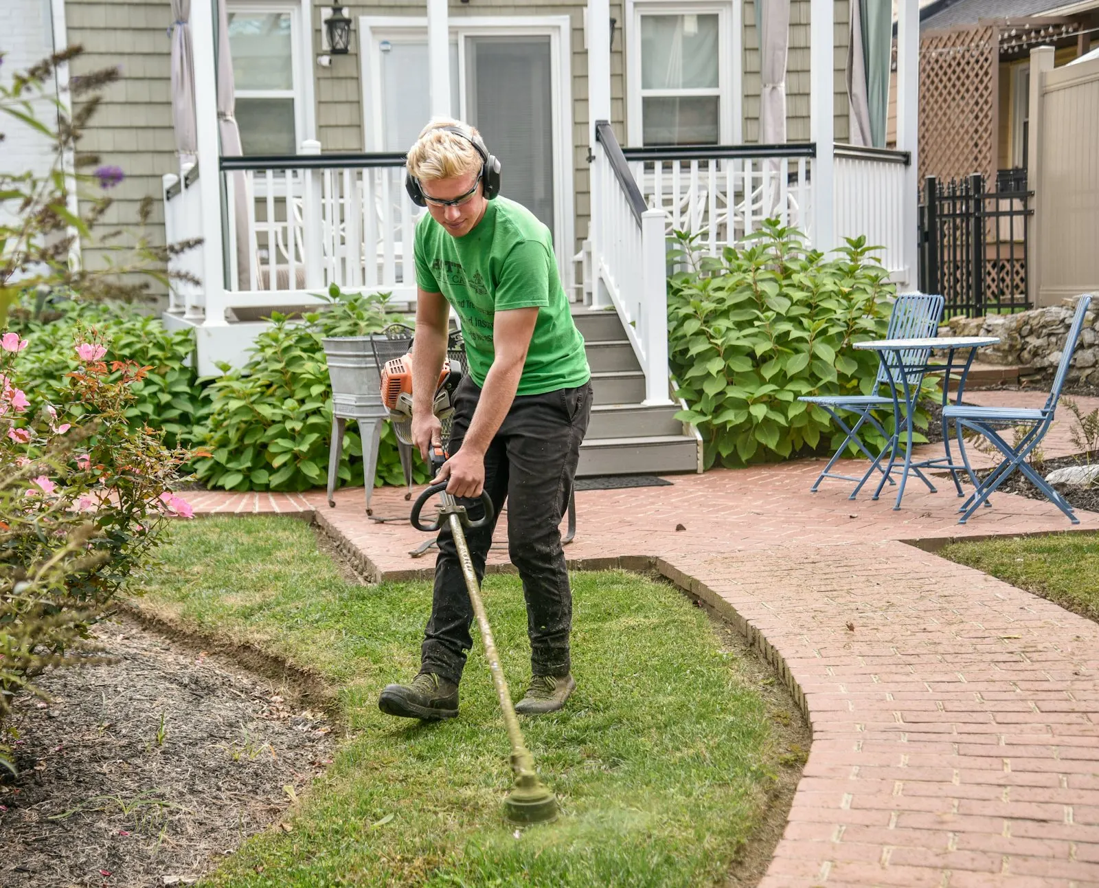 String trimmer cleaning the edge between a sidewalk and a lawn.